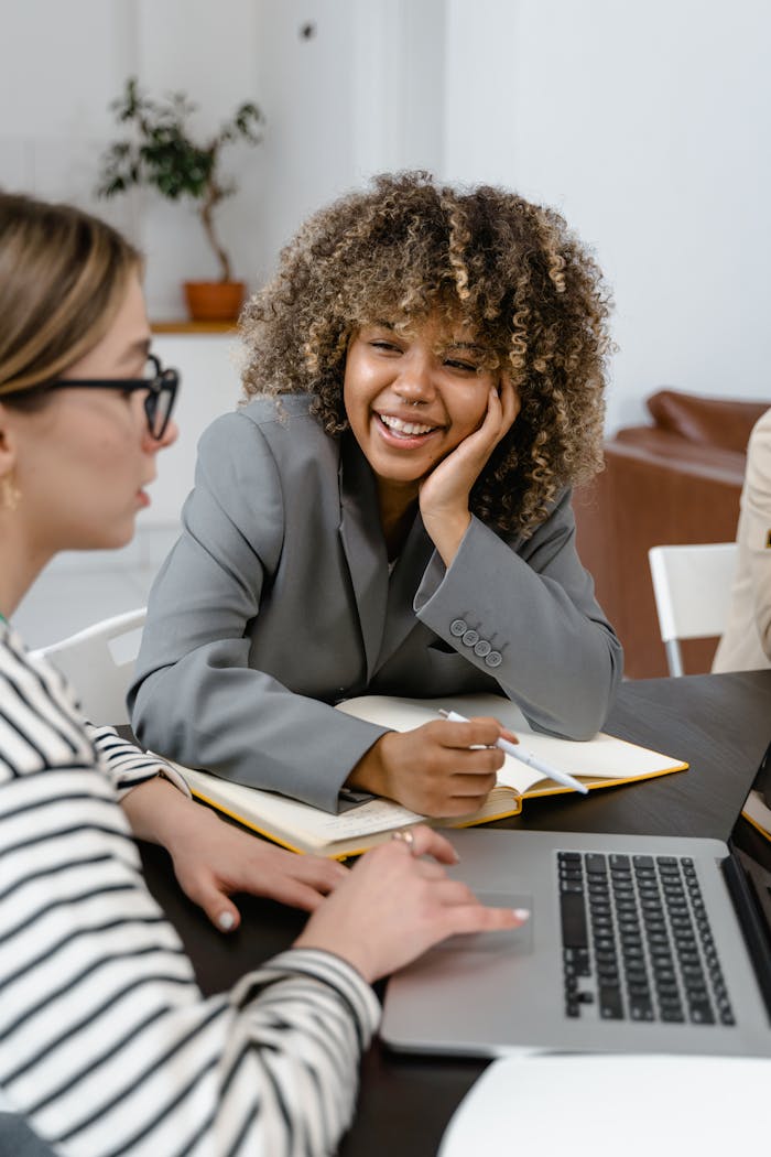 Professional women collaborating in a modern office setting with laptops and notes.